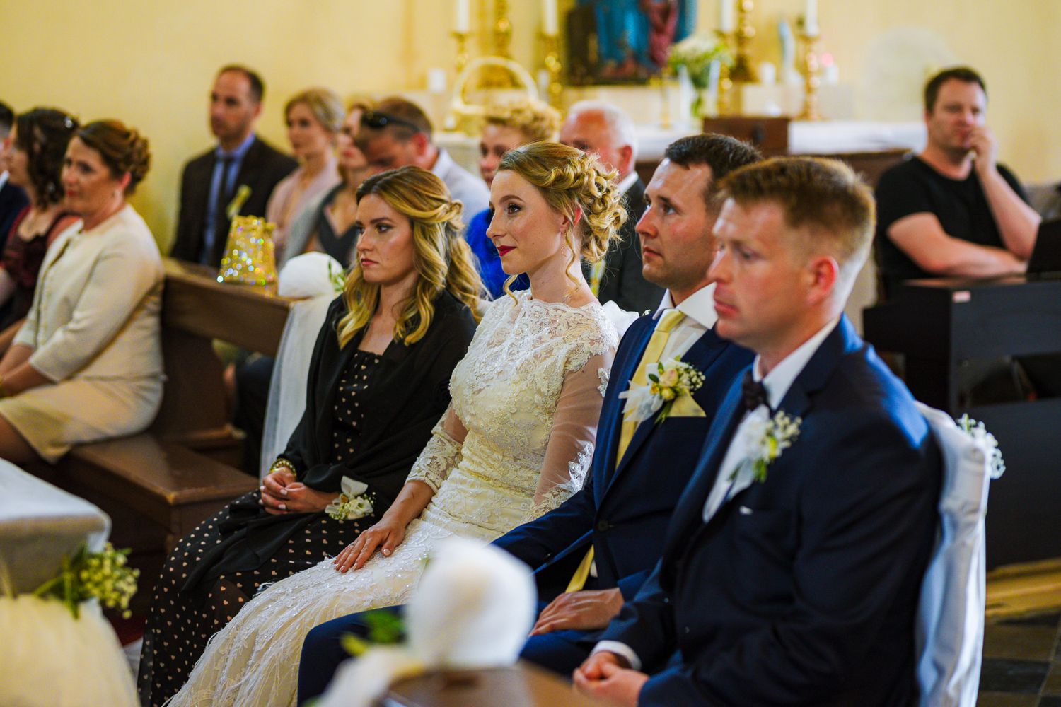 Wedding guests and bridal party seated in church pews during a traditional wedding ceremony.