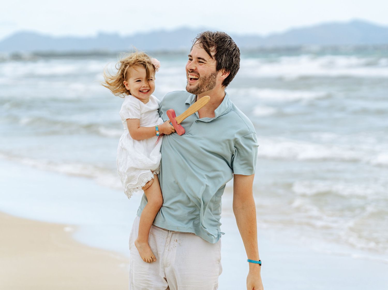 Cheerful dad carrying his laughing little girl on his back along a sunny beach.