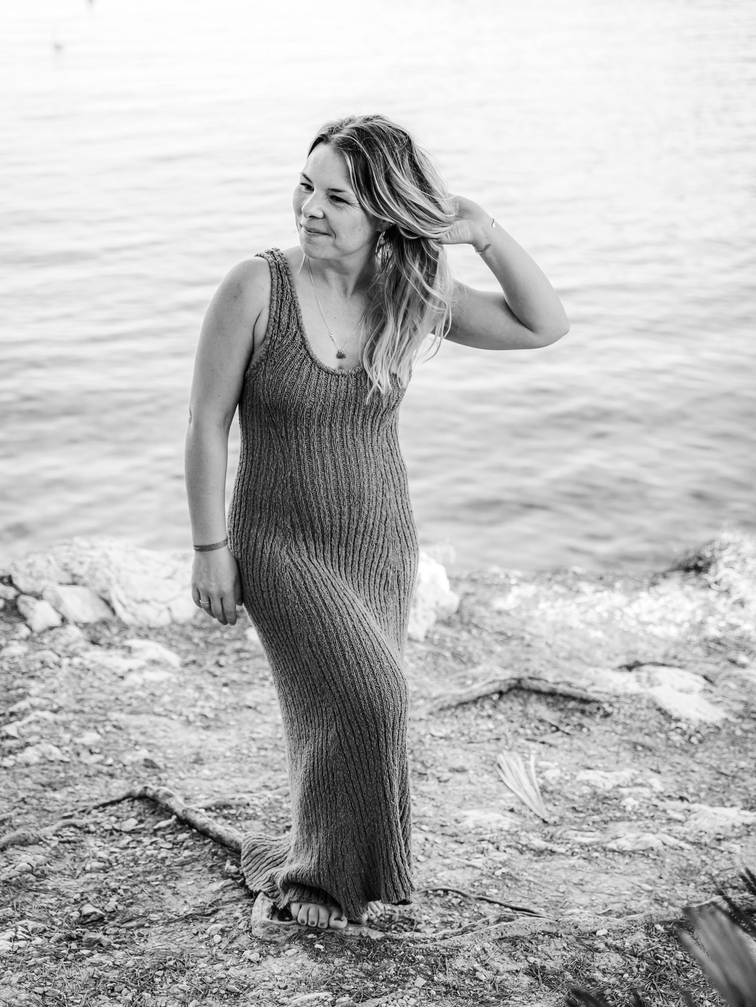 Black and white portrait of a woman in a ribbed maxi dress standing by the sea.