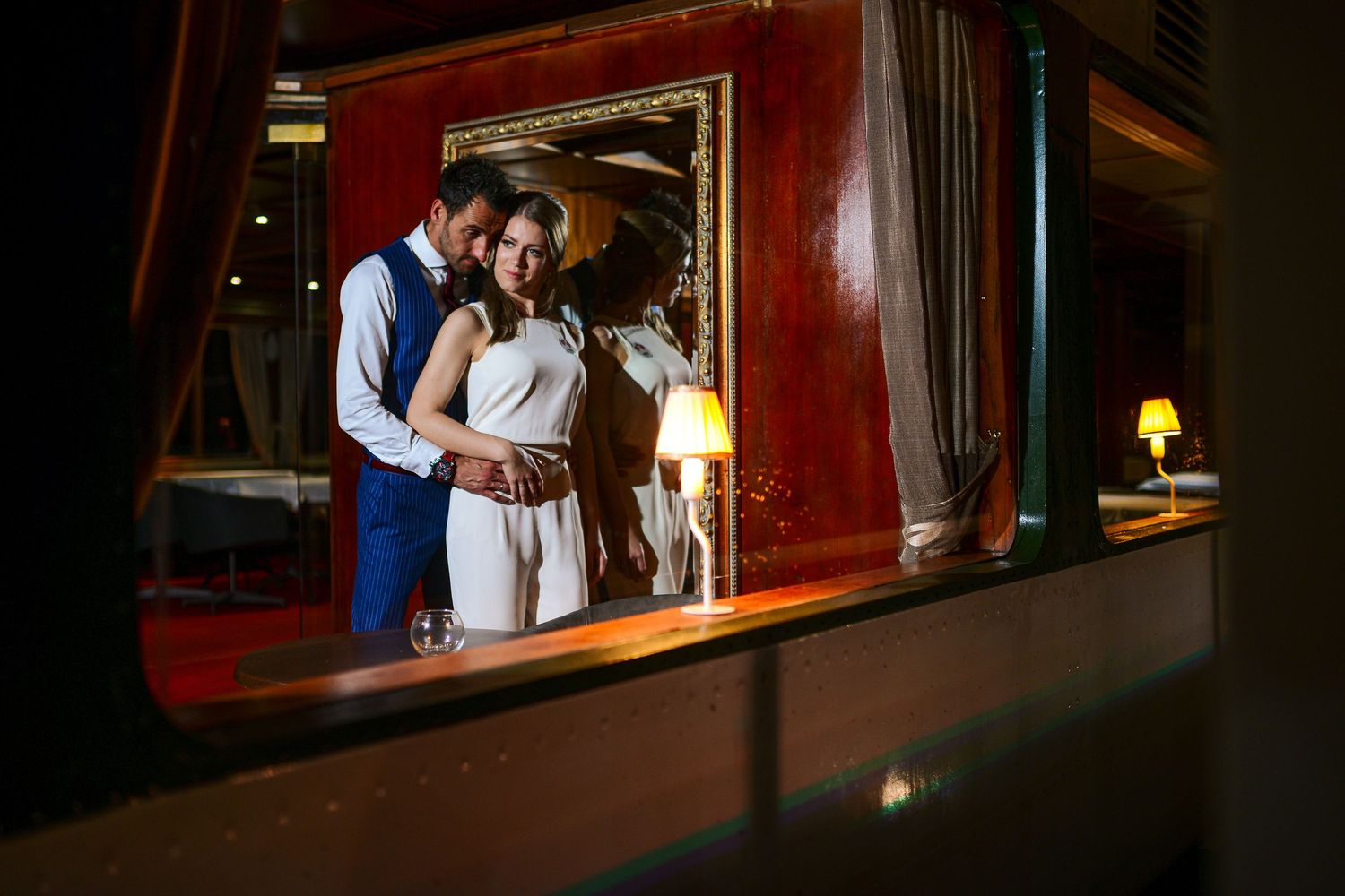 Romantic couple embracing in an elegant warmly lit room with ornate gold mirror reflection.