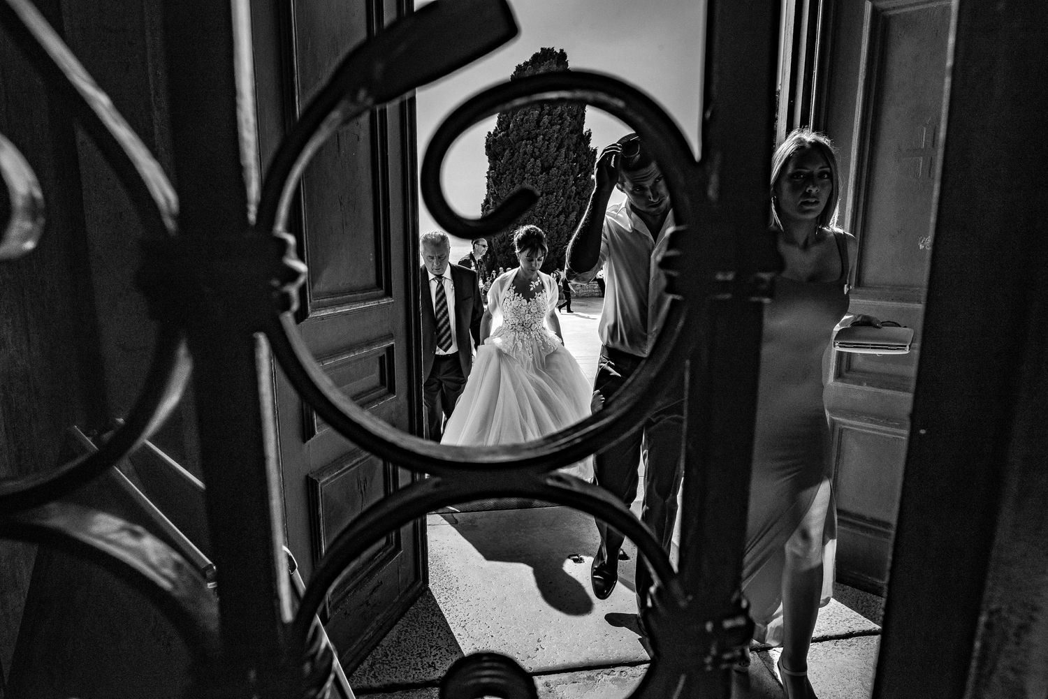 Black and white photo of bride in wedding gown framed by ornate wrought iron staircase.