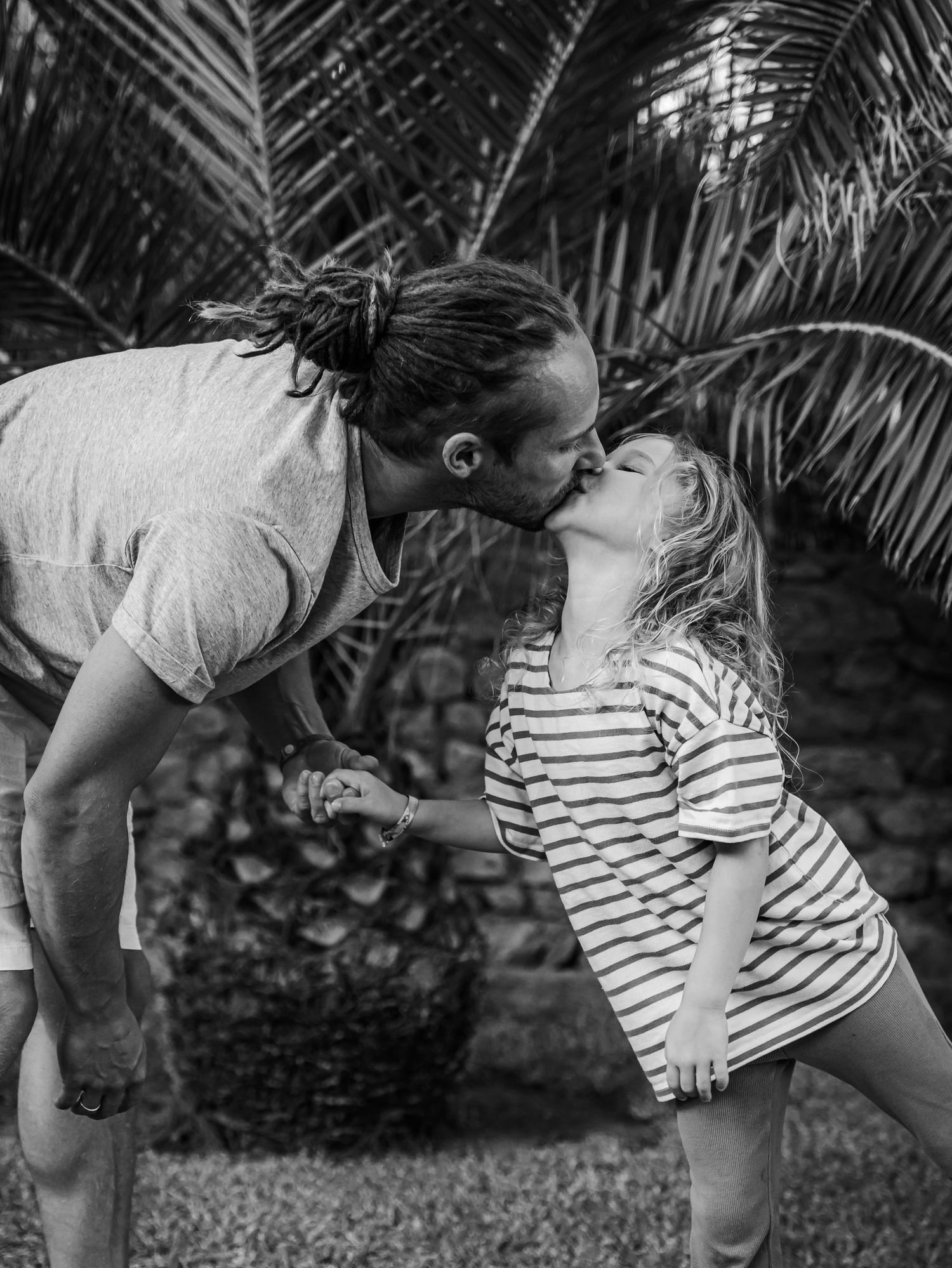 Couple sharing a romantic kiss outdoors near tropical palm trees in black and white photography.