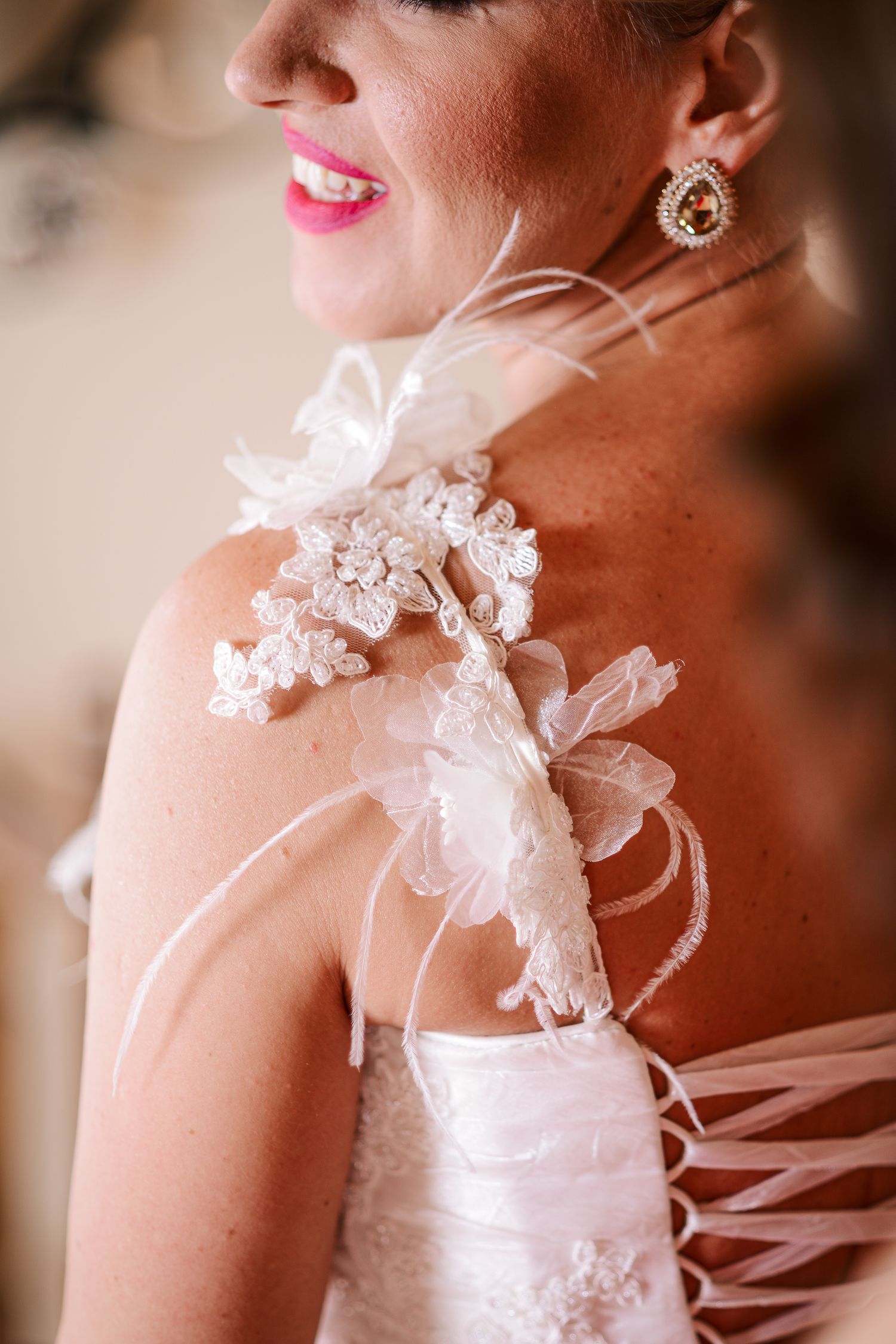 Close-up of a brides lace and feather wedding dress strap detail with a sparkling earring.