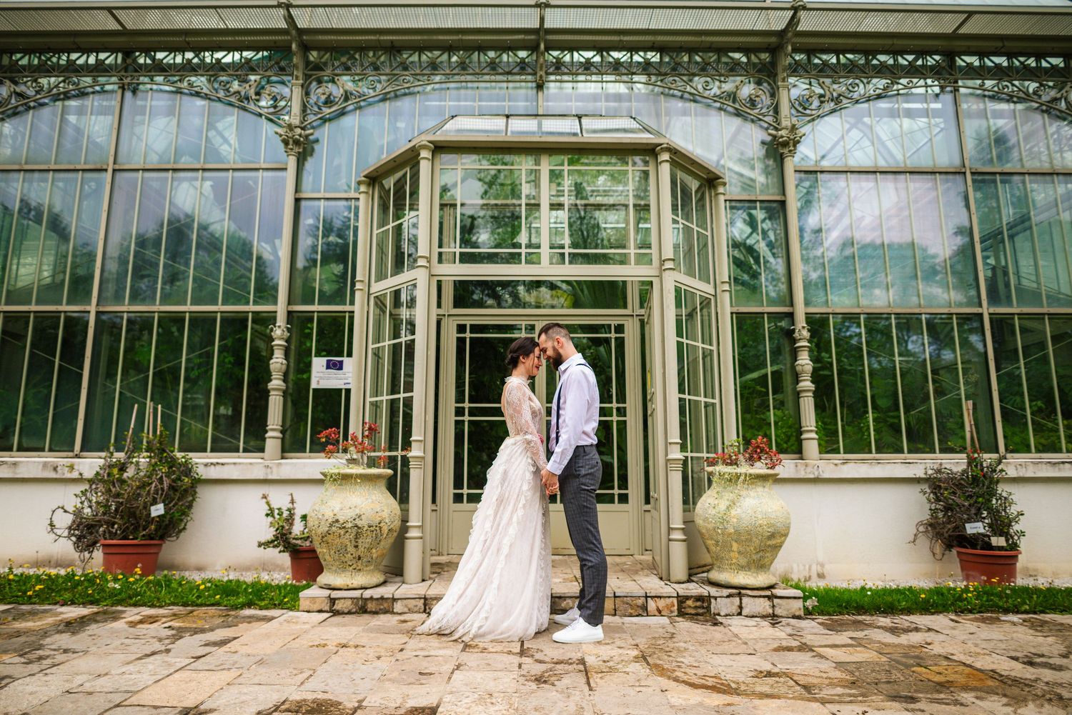 Newlyweds share a tender kiss in front of a stunning ornate glass greenhouse on wedding day.