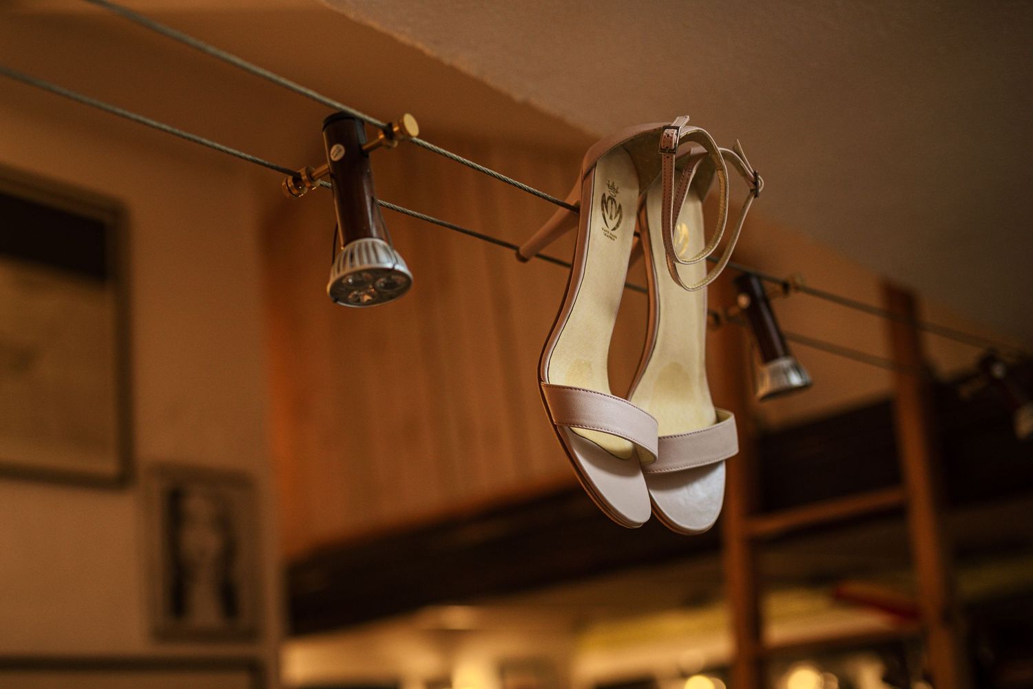 White bridal heeled sandals hanging on a rail under warm spotlights indoors.