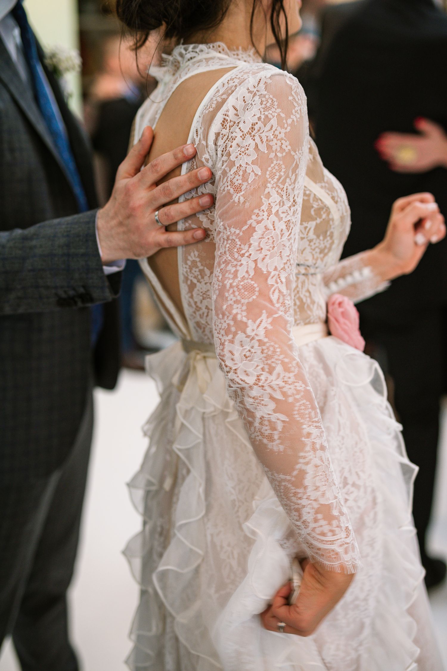 Close-up of bride's intricate lace backless wedding gown with ruffled skirt during first dance.