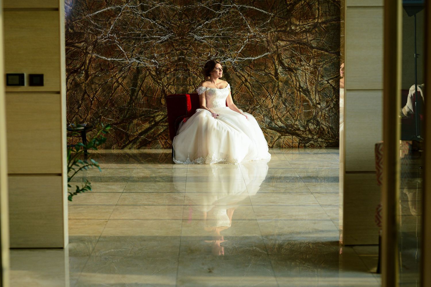 Elegant bride in a voluminous white ball gown seated in a luxurious marble-floored venue.