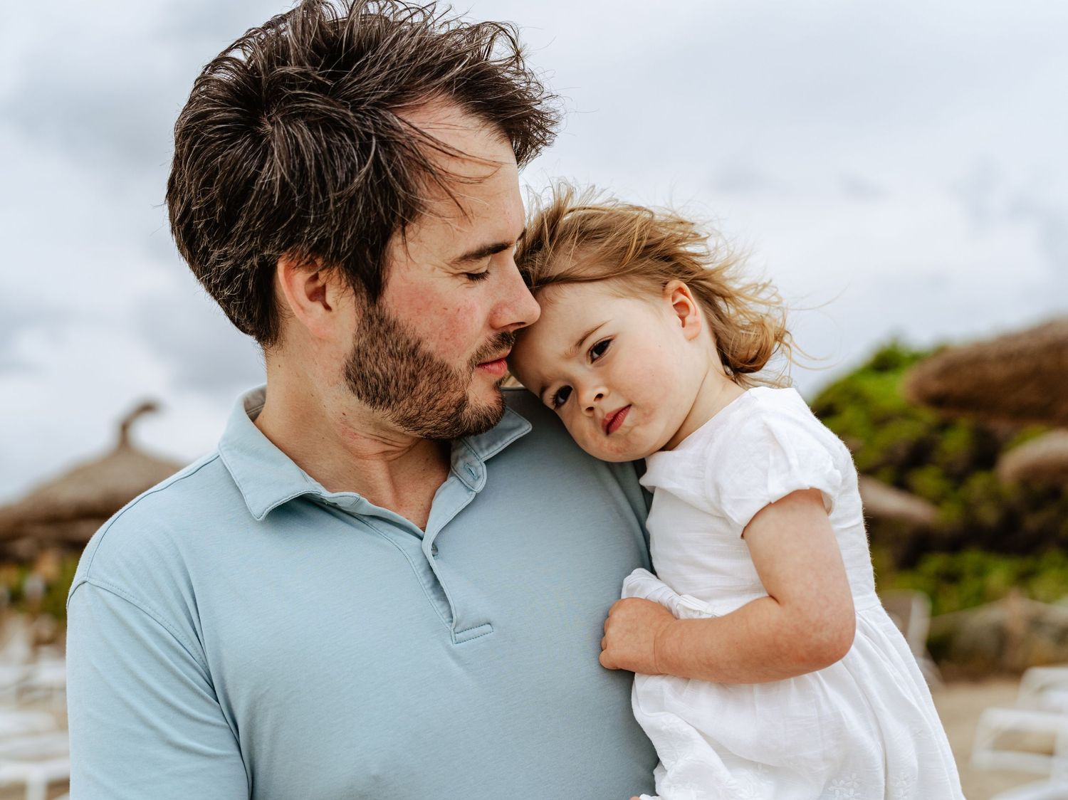 Father tenderly holding sleepy toddler at the beach.