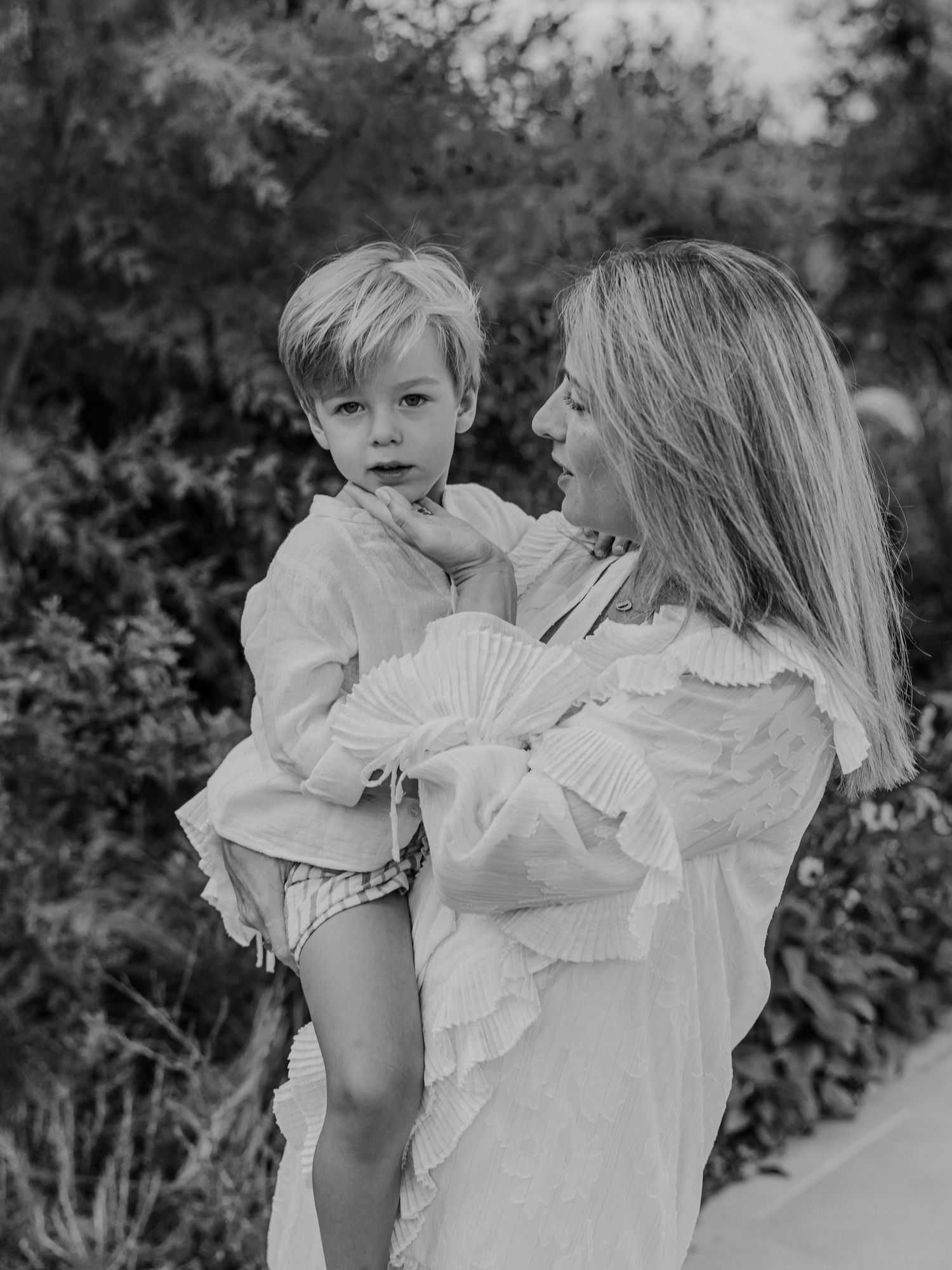 Black and white photo of a mother holding her young son in an outdoor garden.