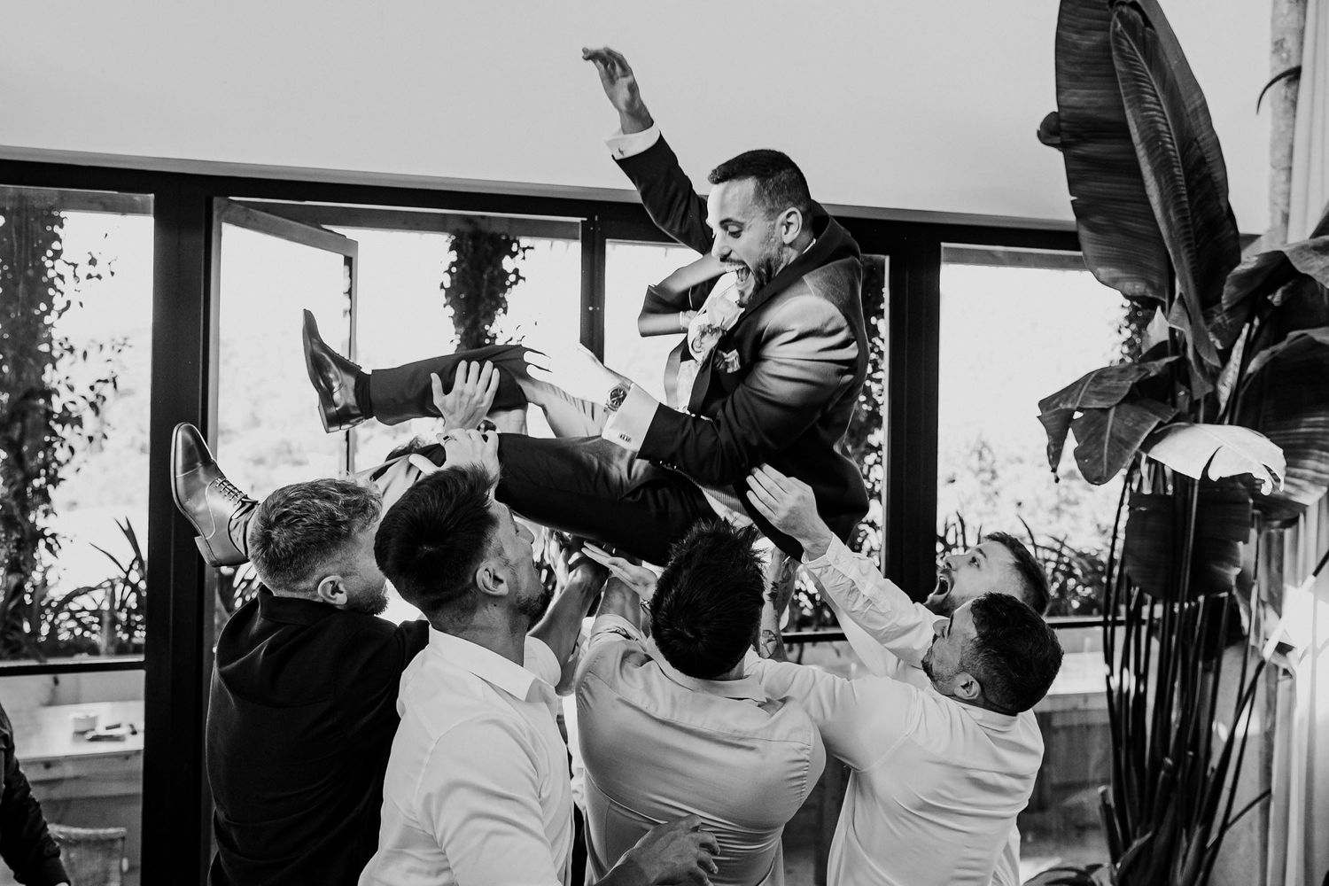Groom being lifted by groomsmen in celebratory toss at wedding reception.