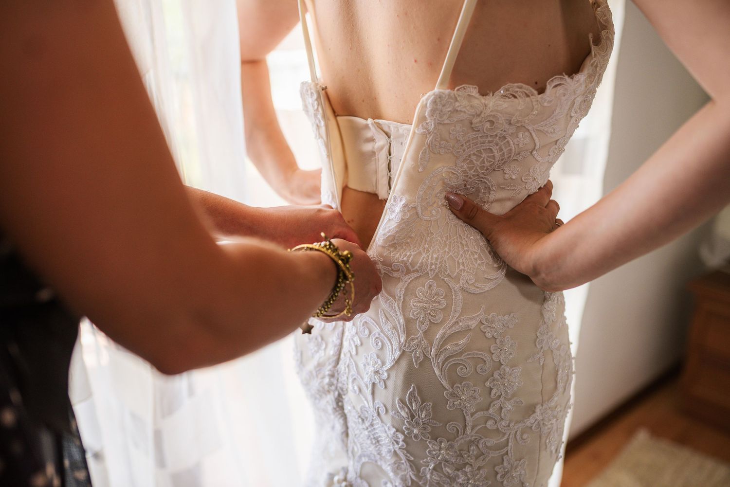 Close-up of hands fastening buttons on back of intricate lace wedding gown.