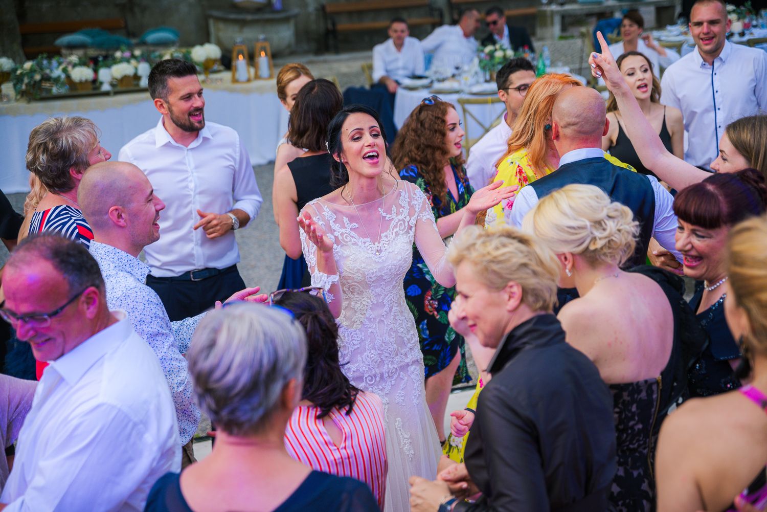 Bride dancing joyfully with wedding guests on crowded reception dance floor.