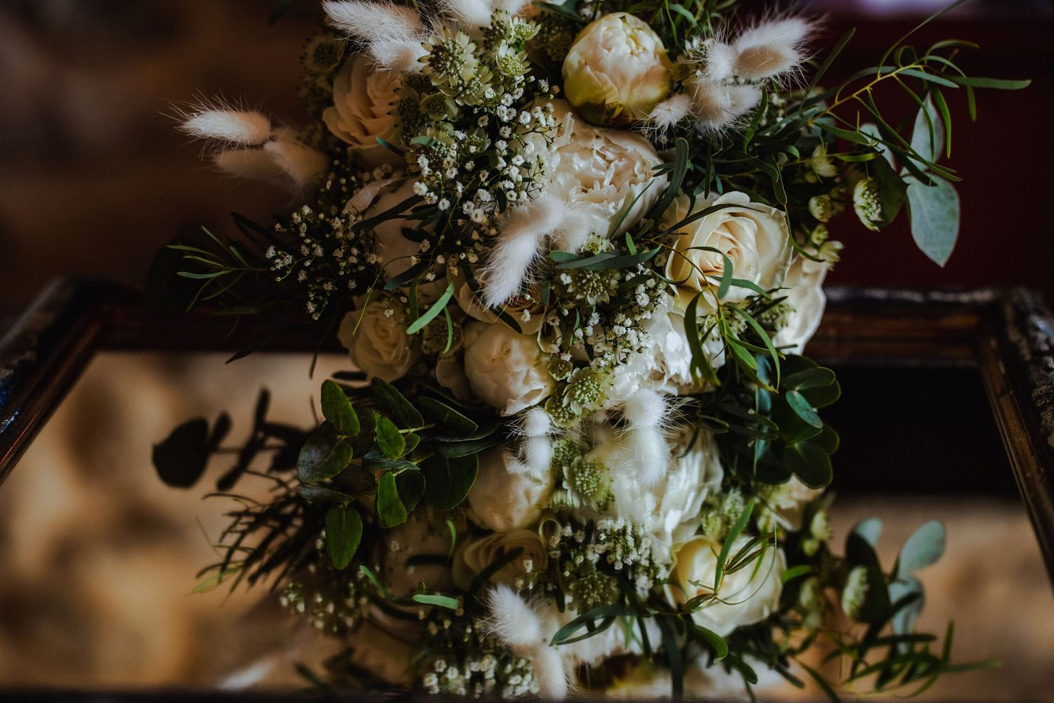 Close-up of a bridal bouquet with white roses, greenery, and dried pampas grass.