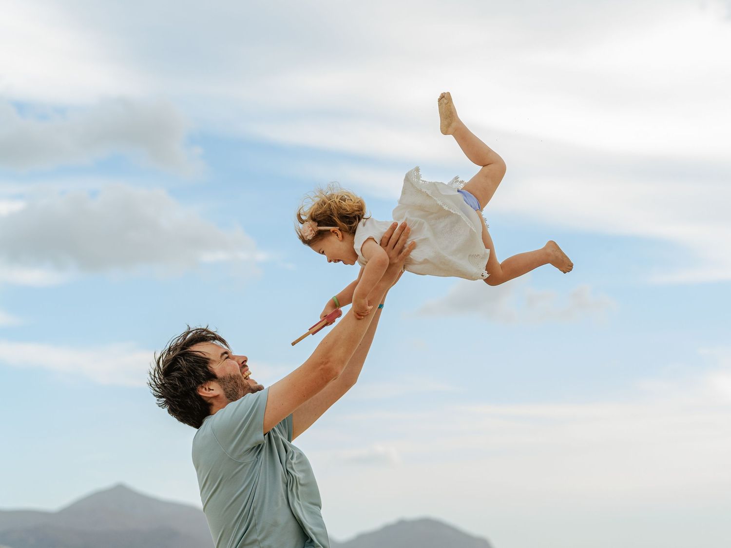 Father tossing laughing child into sky outdoors.
