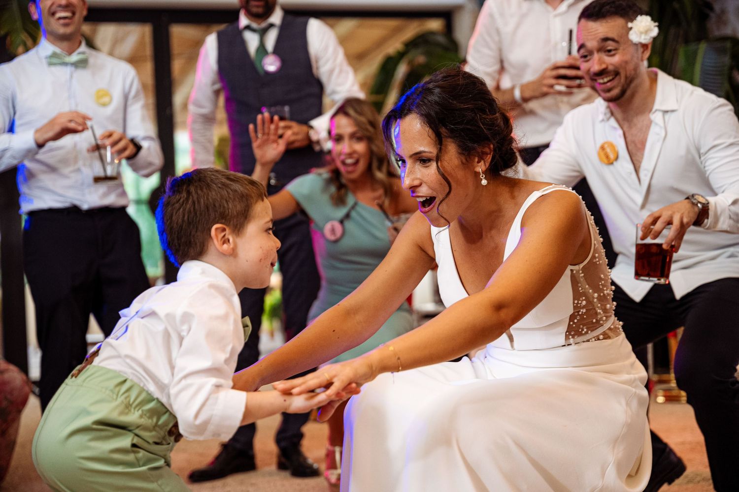 Bride in white gown joyfully interacting with a young child on the dance floor at a wedding reception.