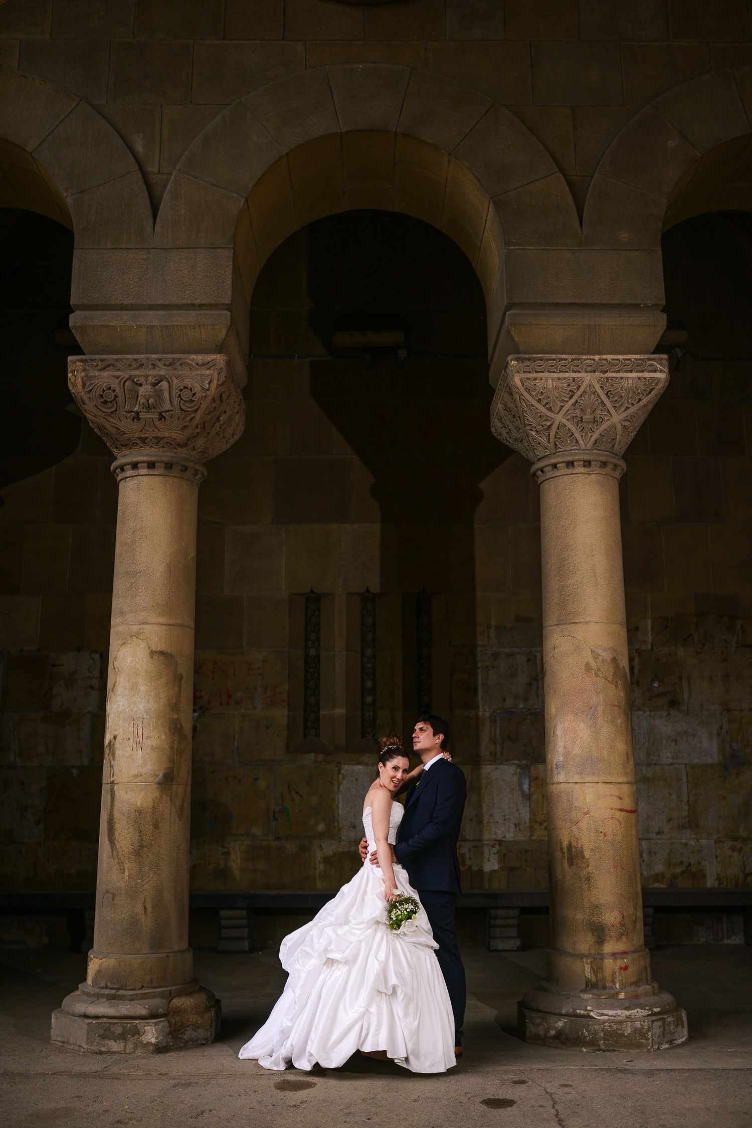 Weddong couple emvracing beneath historic stone arches, timeless wedding photography by Herzenshaus Studio, Frankfurt Rhein-Main.
