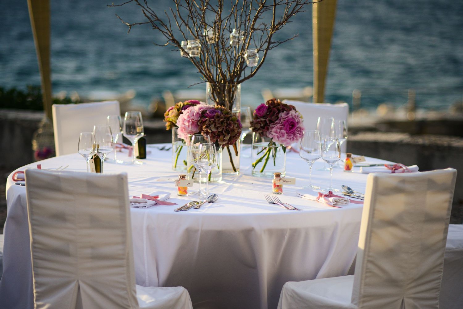 Elegant wedding reception table decorated with pink flowers, glassware and rustic branch centerpiece for an outdoor wedding celebration.