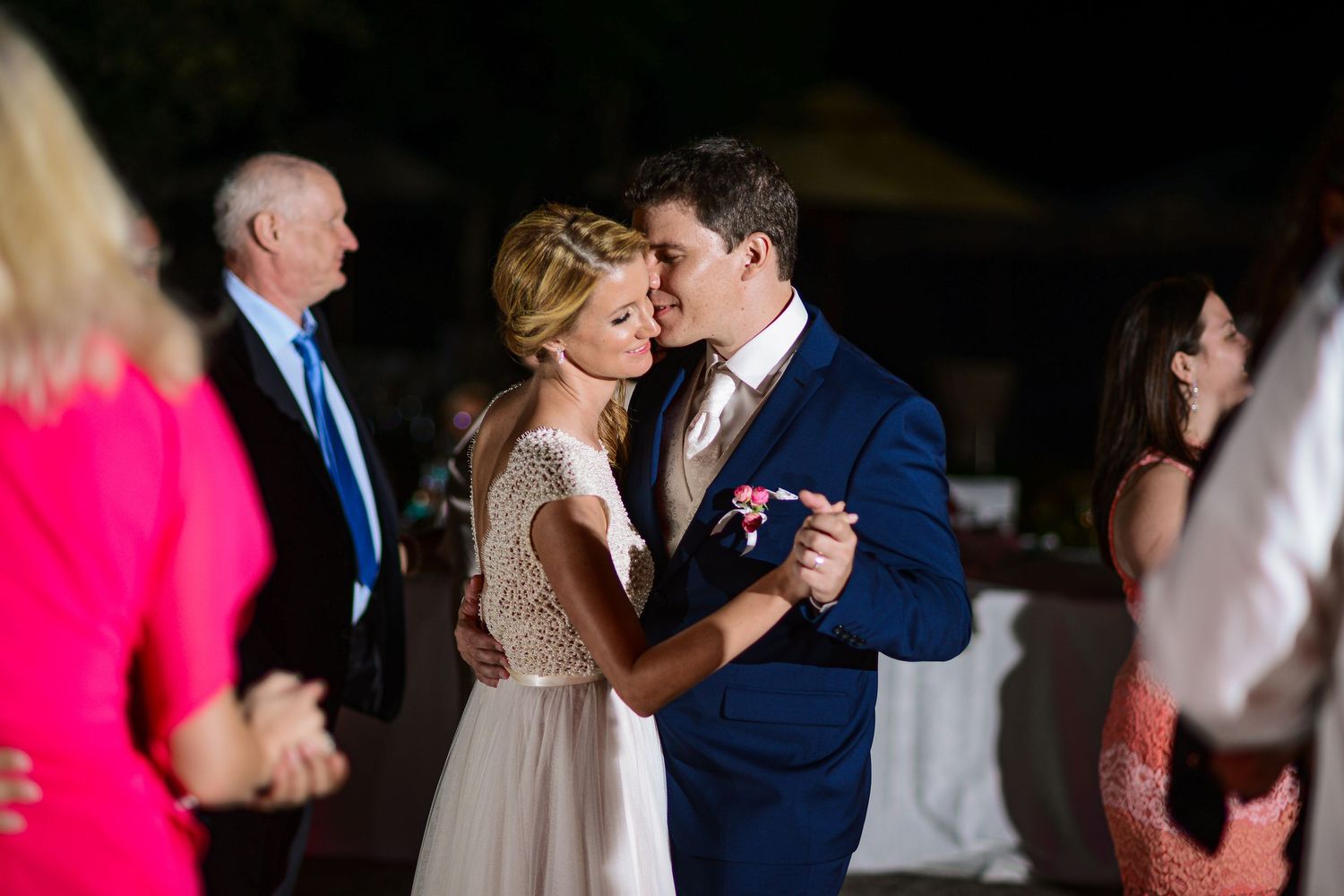Bride and groom sharing first dance surrounded by guests at romantic outdoor evening wedding reception.