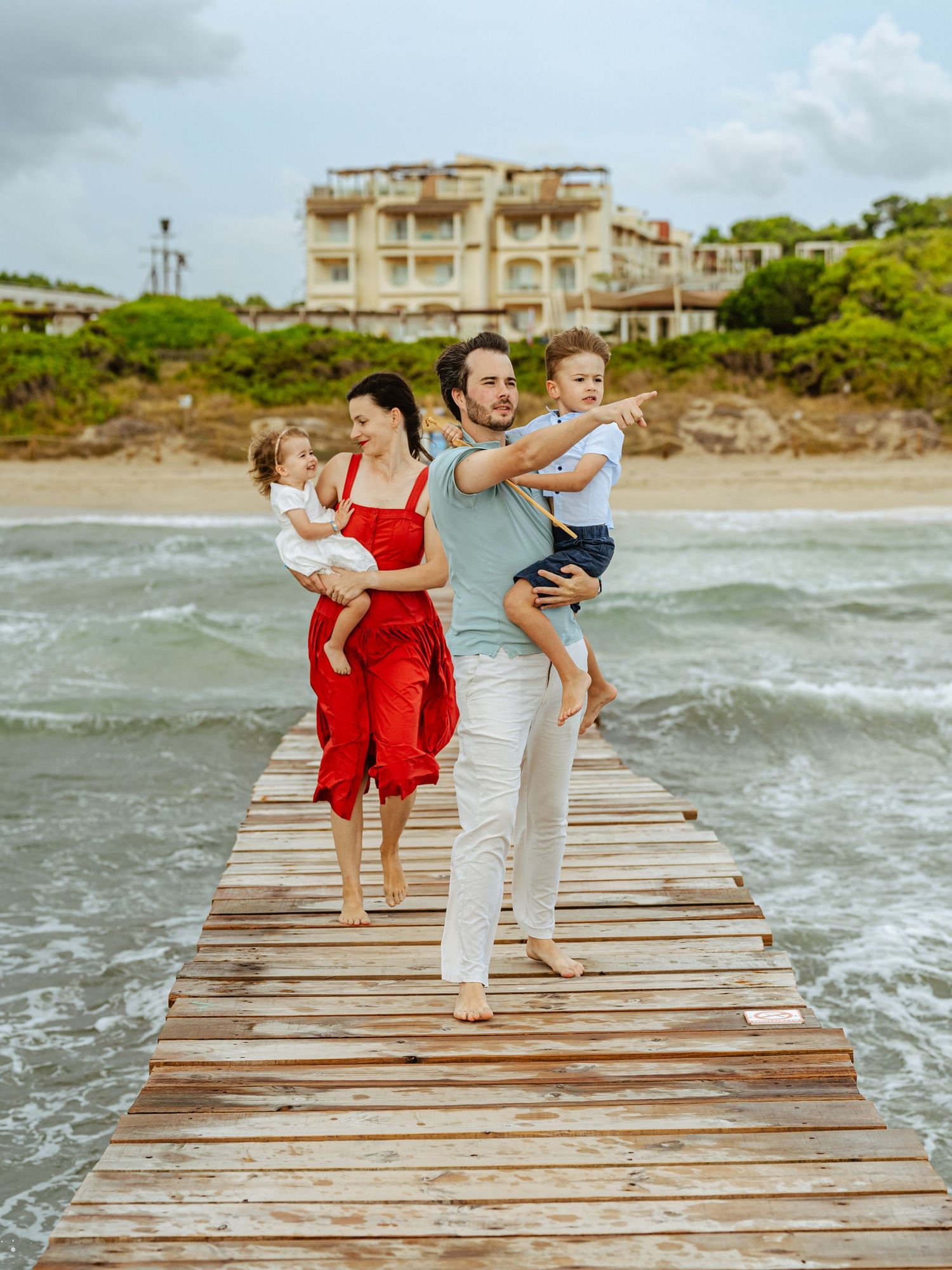 Family of four with two young children standing on a wooden pier by the ocean.