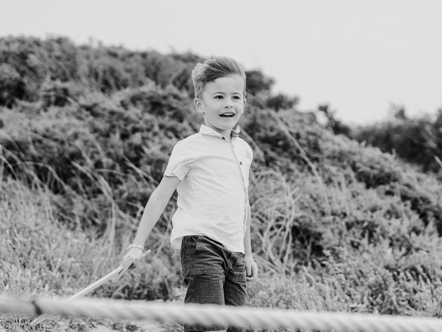 A happy young boy laughs while walking outdoors in a black and white photo with greenery in the background.