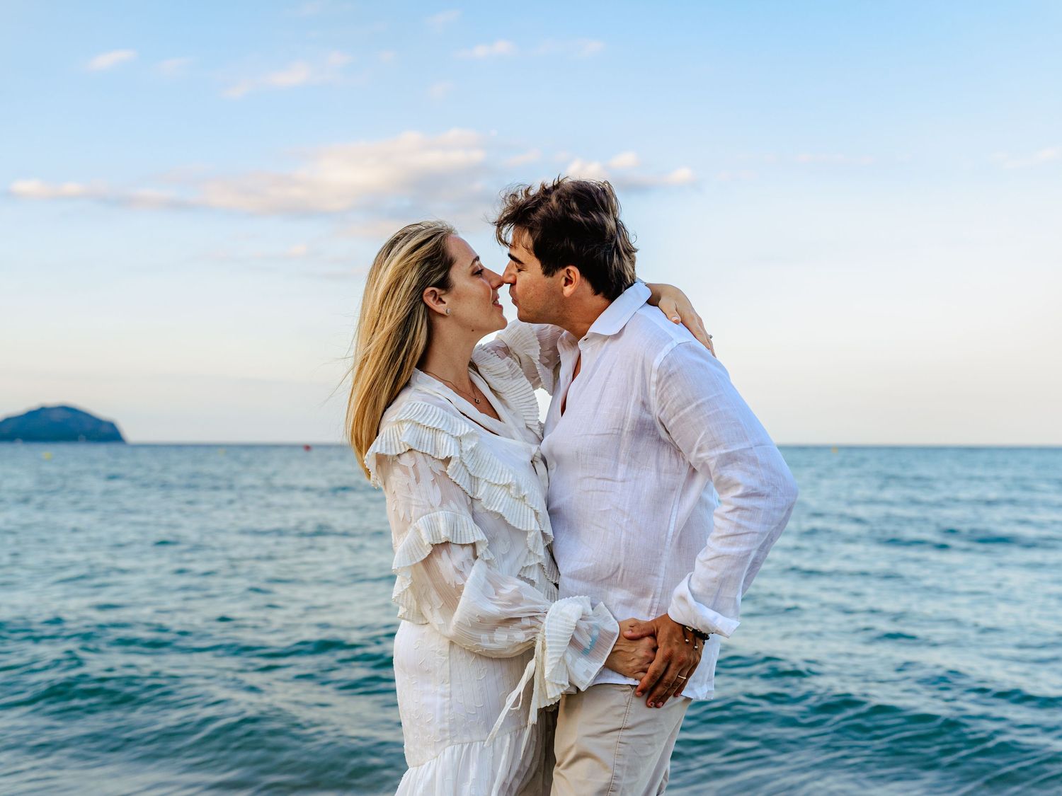 Romantic couple kissing on a beach with turquoise ocean and island in background.