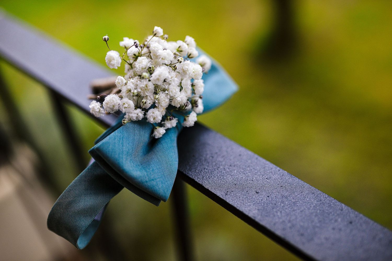 White baby's breath boutonniere tied with teal ribbon resting on dark metal railing.