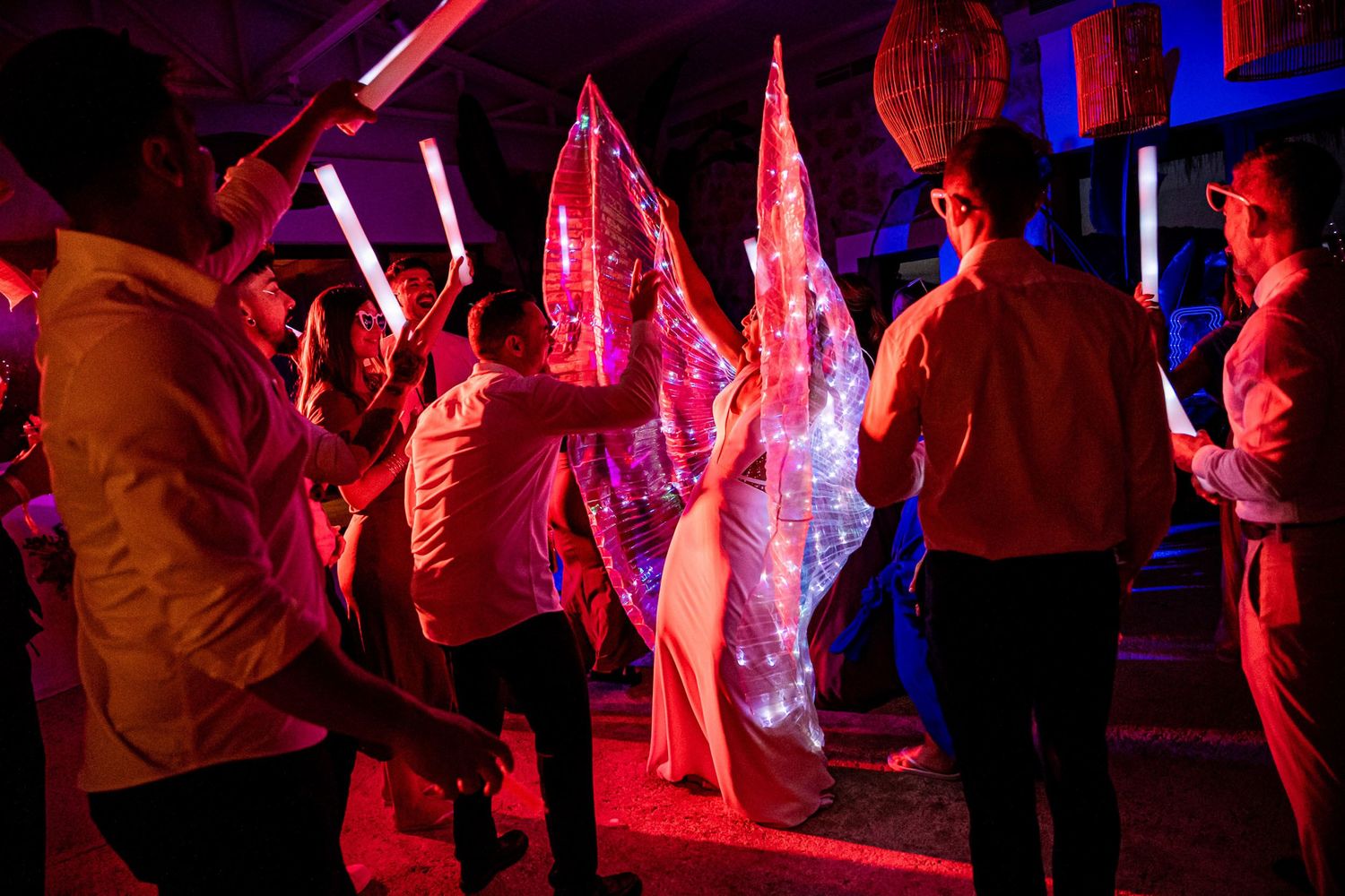 Wedding guests dance with glowing LED light sticks at a vibrant neon-lit reception party.