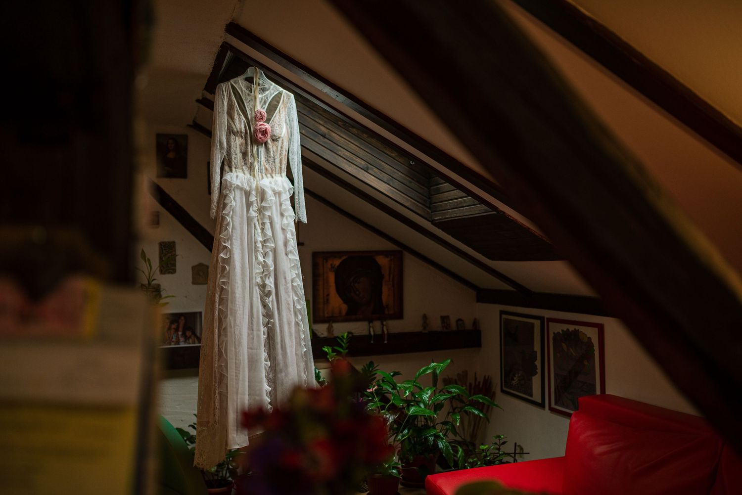 White wedding dress hanging in an attic room with warm lighting and artwork on the walls.
