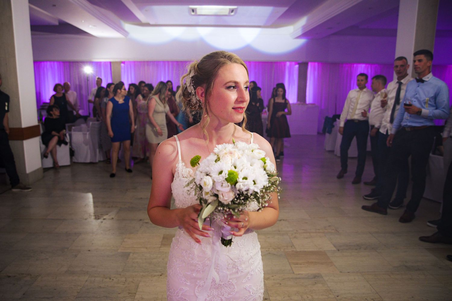 Beautiful bride holding white bouquet while standing on wedding reception dance floor.
