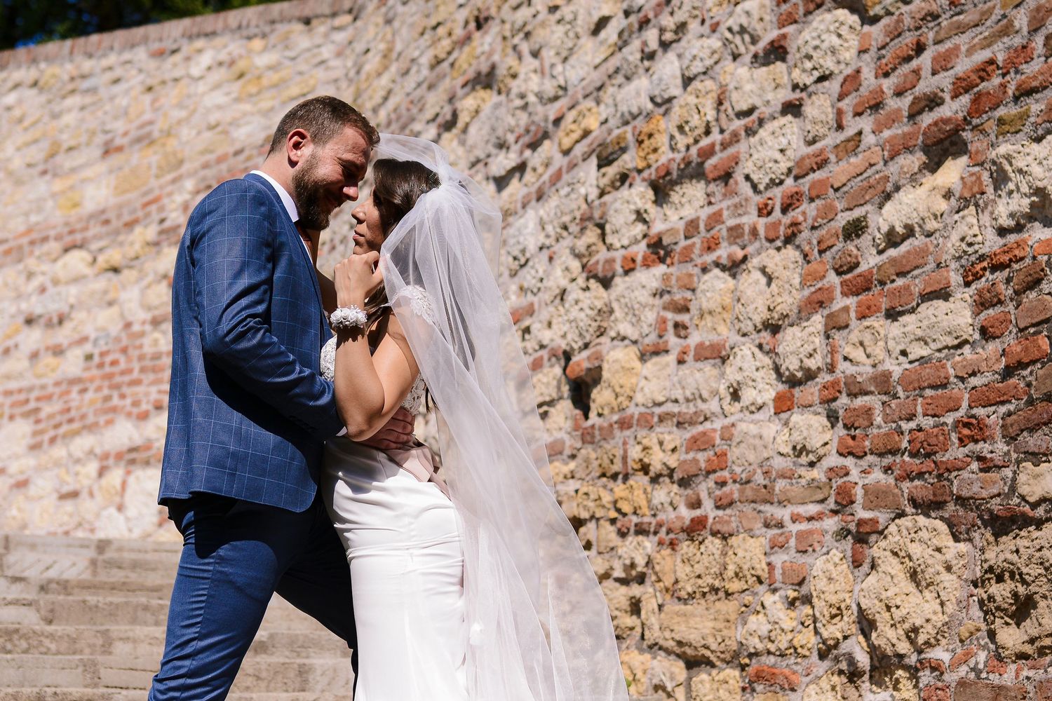 Bride and groom sharing an intimate moment against a rustic brick wall on their wedding day.