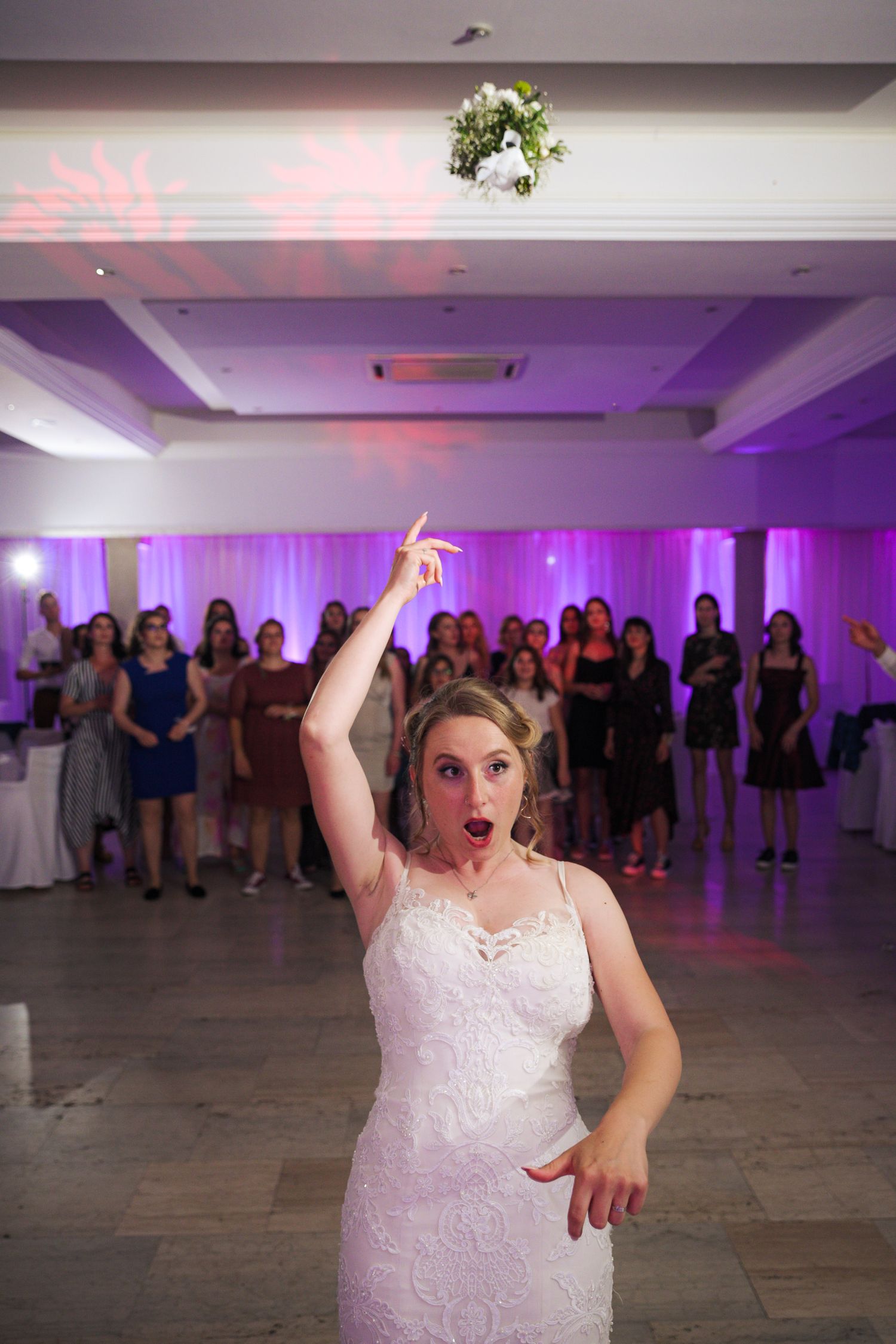 Bride tossing her bridal bouquet to waiting guests at wedding reception.