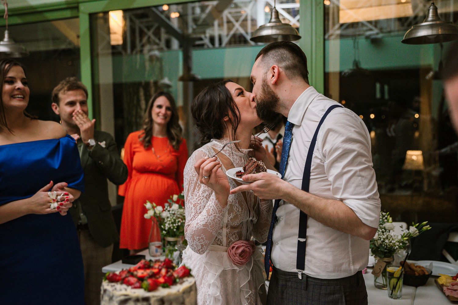 Newlyweds share a romantic kiss while feeding each other wedding cake at reception.