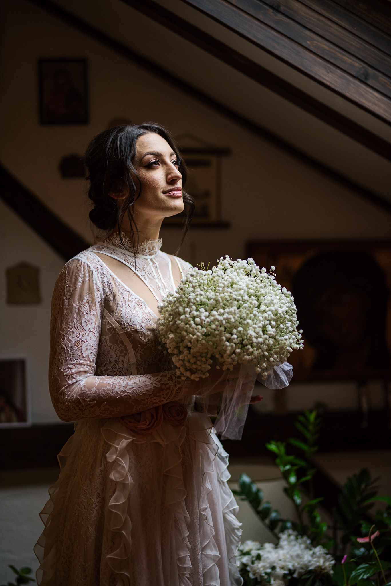 Elegant bride in vintage lace wedding dress holding a large white baby's breath bouquet indoors.
