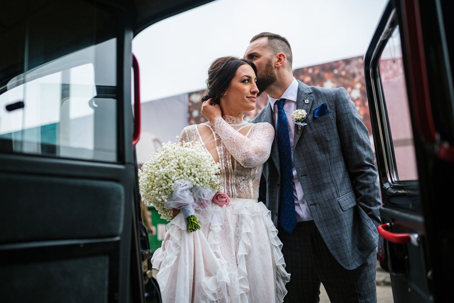 Bride holding her bouquet as the groom kisses her forehead beside their wedding car after the ceremony. By Herzenshaus Studio, Frankfurt.