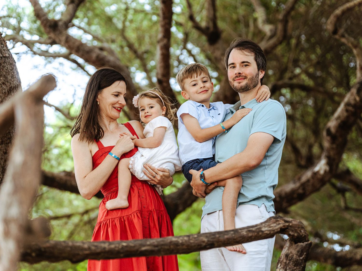 Smiling family of four standing among large tree branches in a sunny outdoor setting.