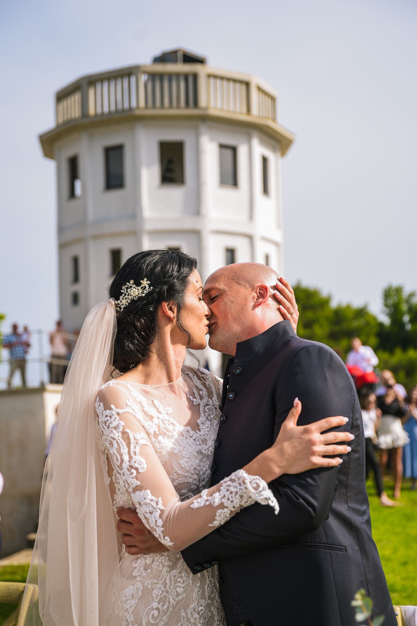 Bride and groom sharing a kiss in front of a white tower at their outdoor wedding ceremony.