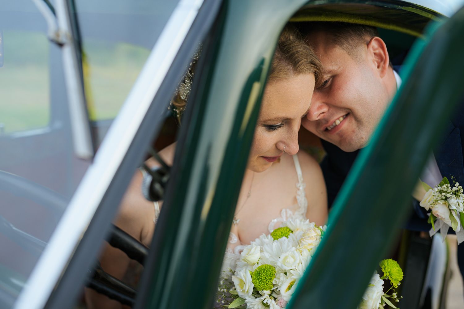 Bride and groom sharing a tender moment inside a vintage classic wedding car.