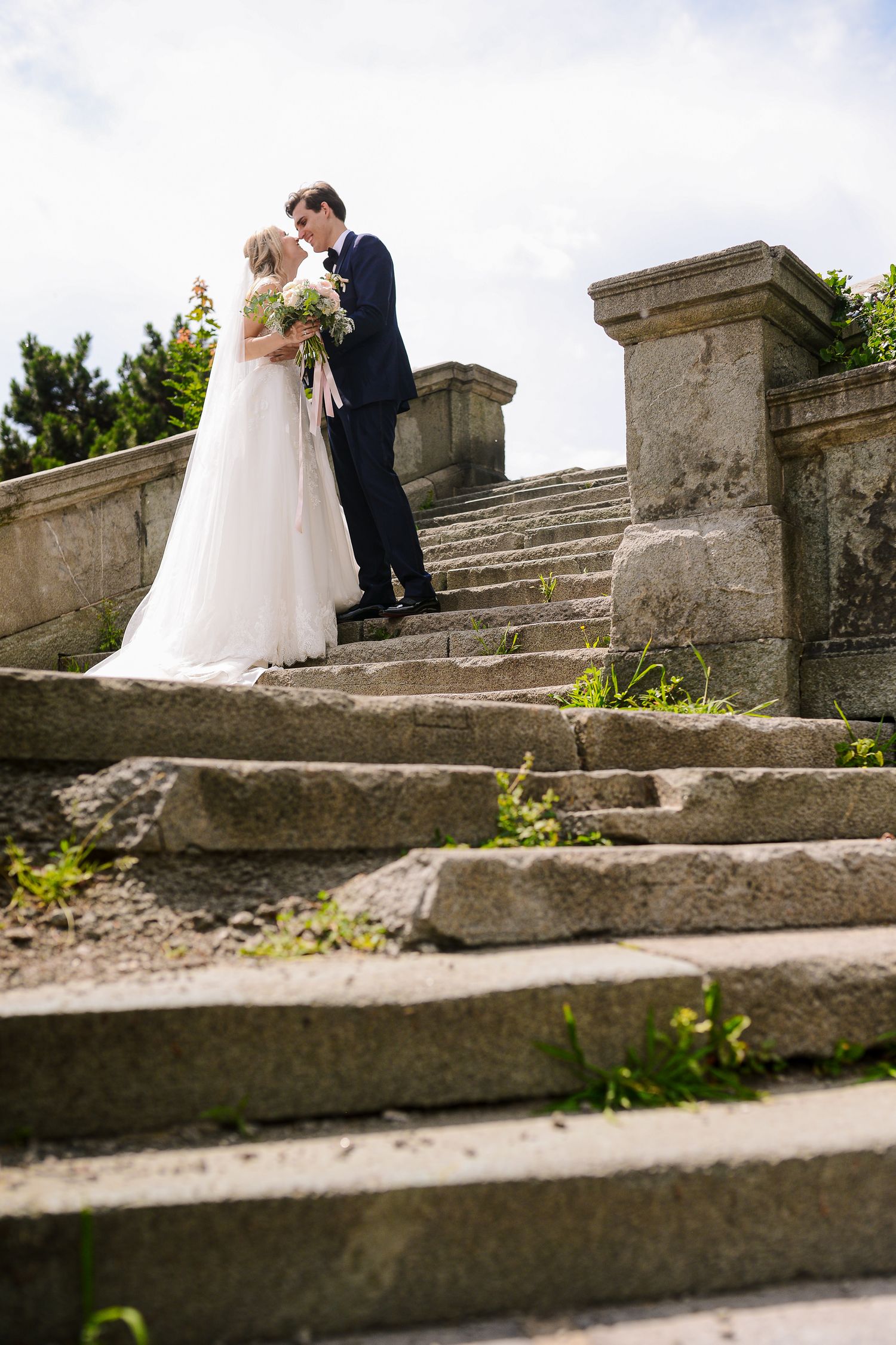 Bride and groom share a romantic kiss at the top of ancient stone steps on their wedding day.