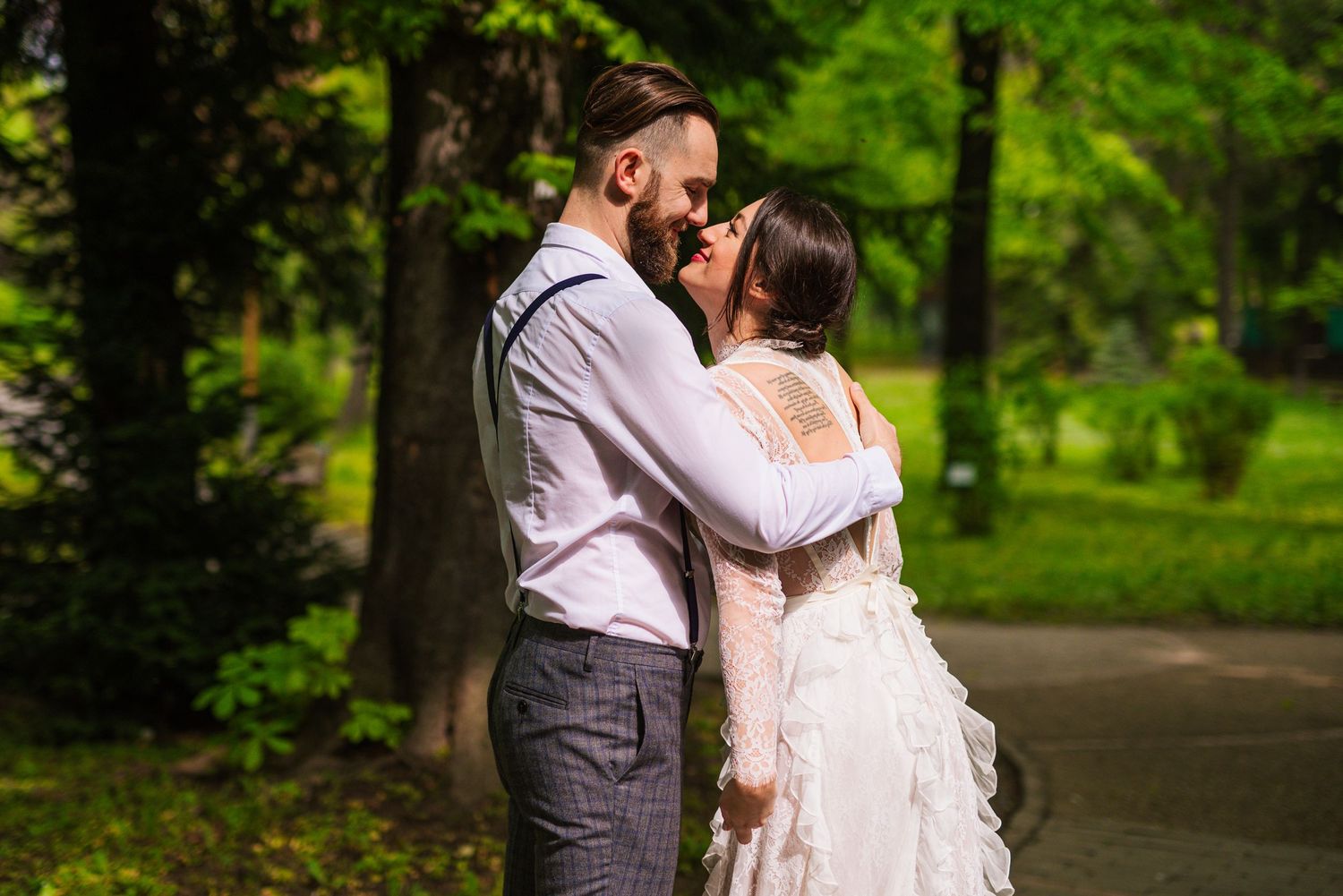Romantic newlyweds nearly kissing while embracing in a sunlit green park on their wedding day.
