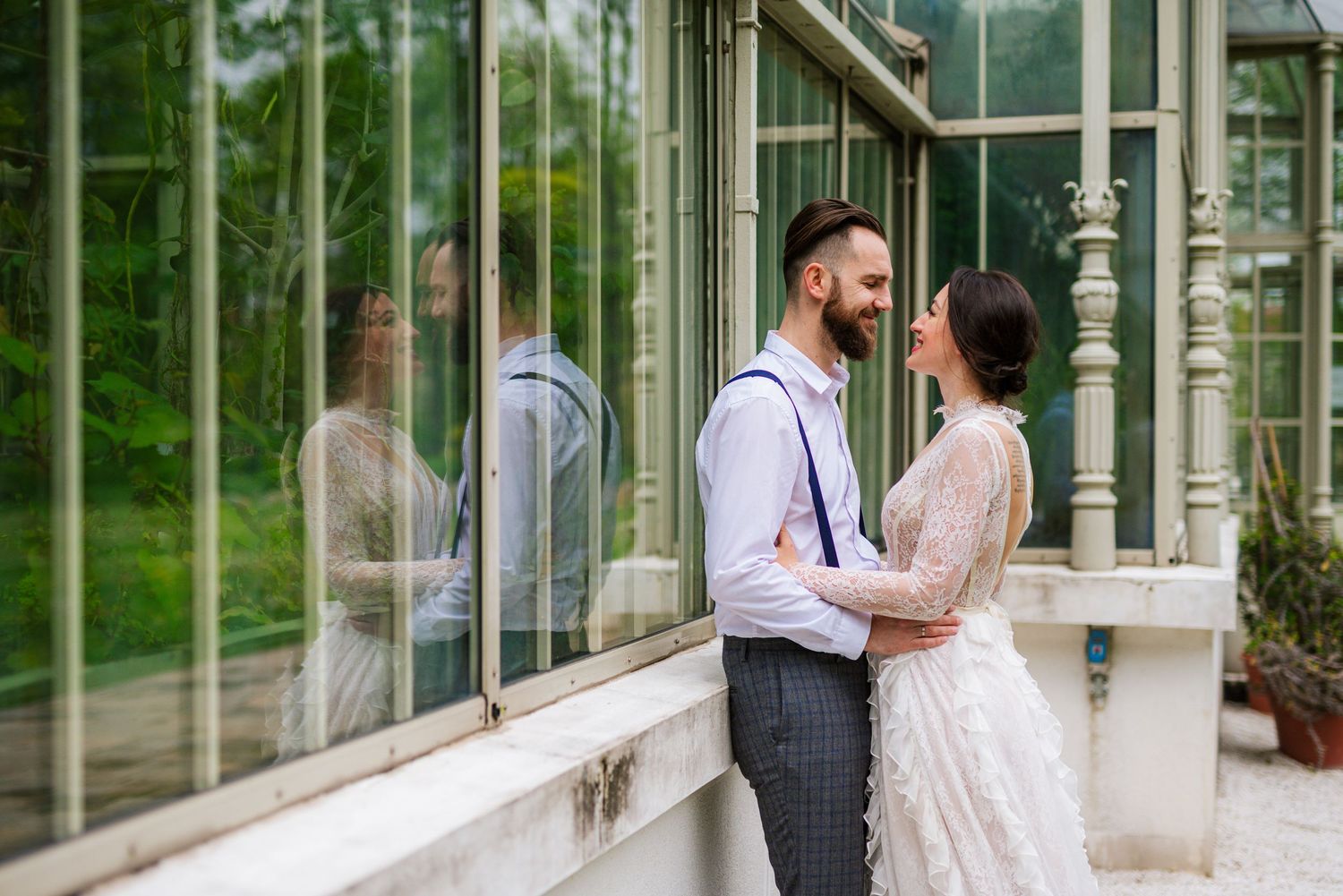Elegant bride and groom share a romantic moment beside a glass greenhouse on their wedding day.