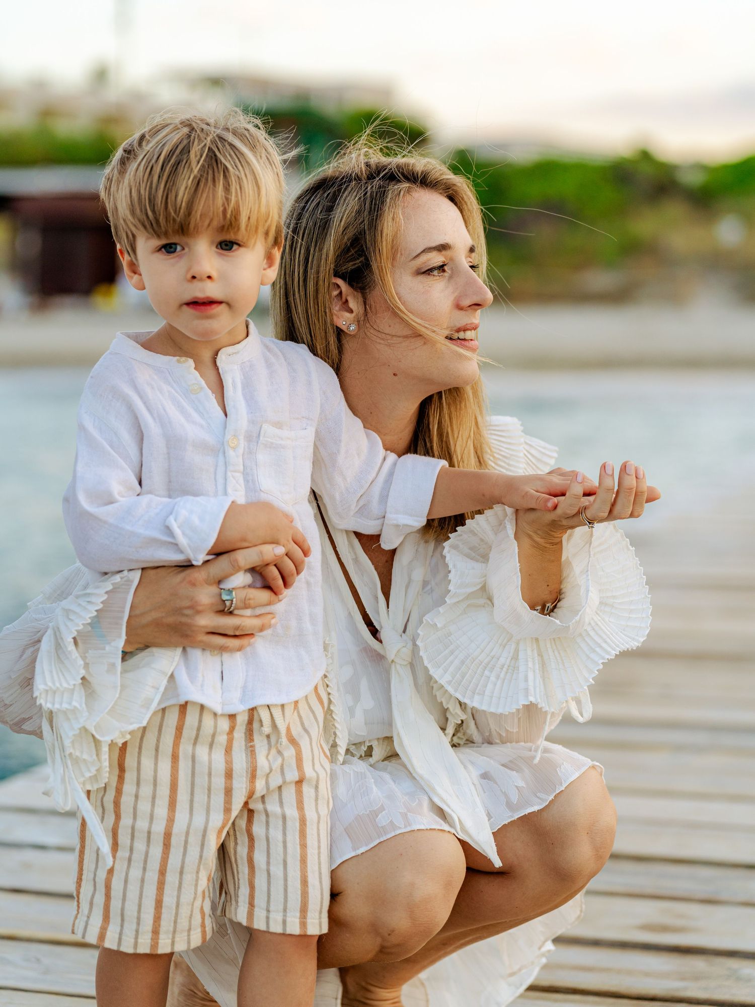 Young mother crouching with her blond toddler son on a seaside dock at golden hour.