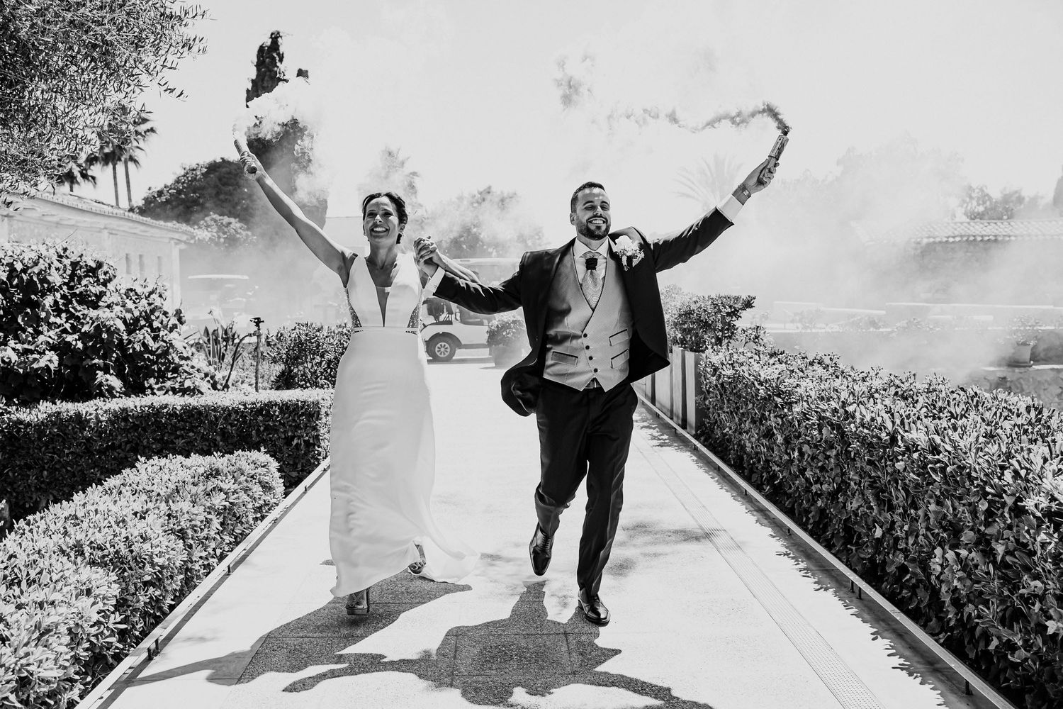 Joyful newlyweds running with smoke bombs in black and white wedding photo.
