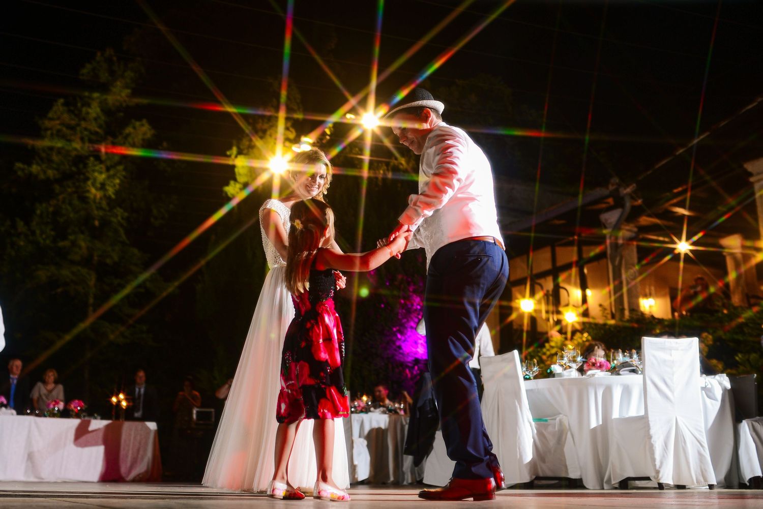 Bride and groom share a first dance under colorful starbursting lights at an outdoor wedding reception.