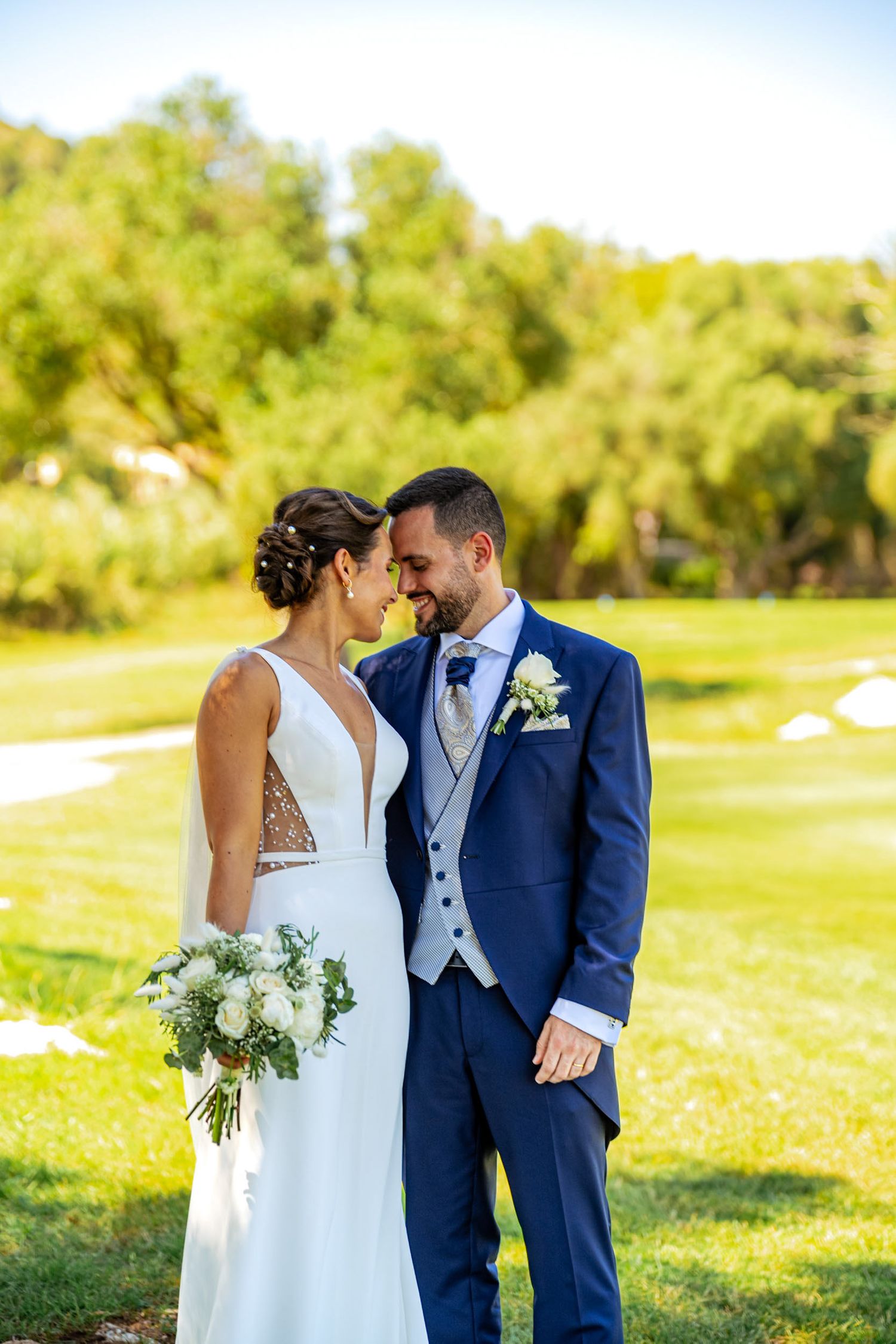 Newlyweds share an intimate nose-to-nose moment on sunny green golf course backdrop.