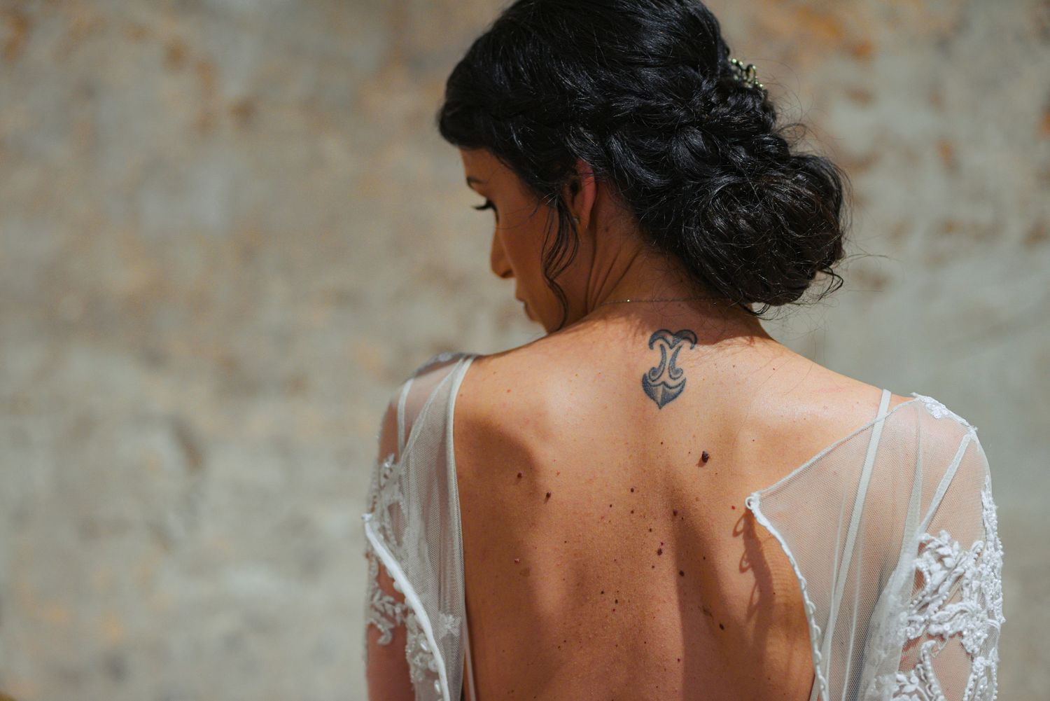 Close-up of brides open-back lace wedding dress revealing elegant tattoo on upper back.