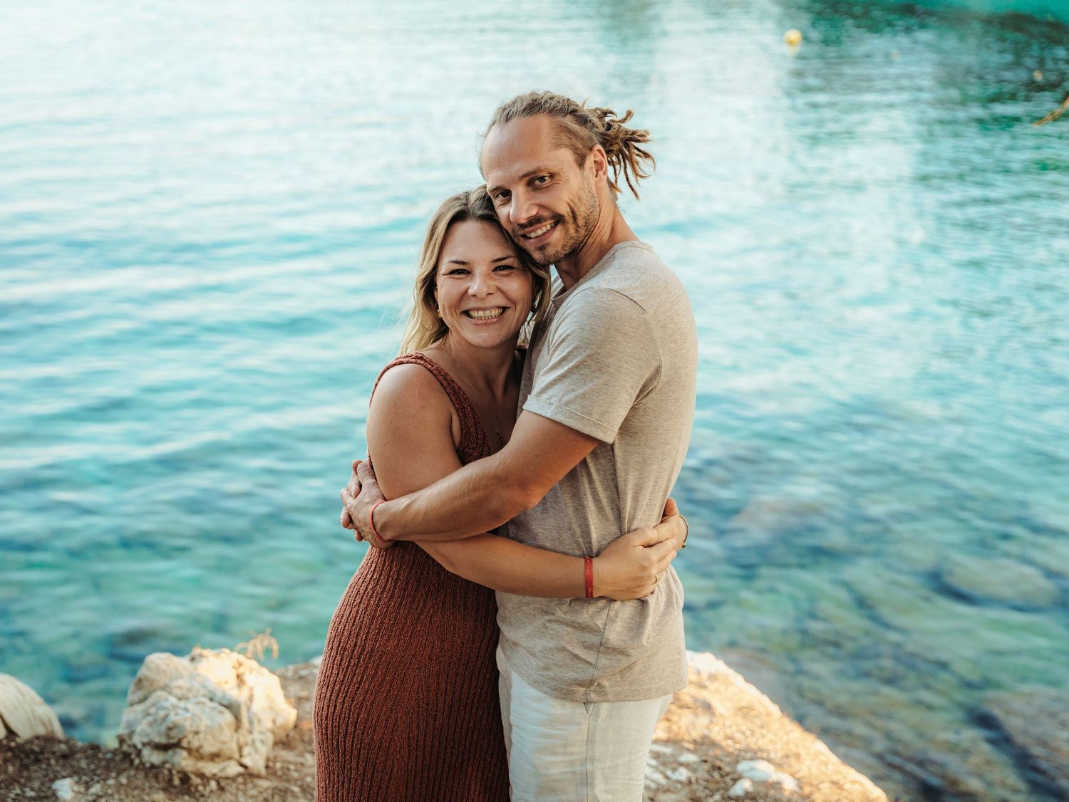 Loving couple embracing and smiling together by turquoise blue water on sunny day.