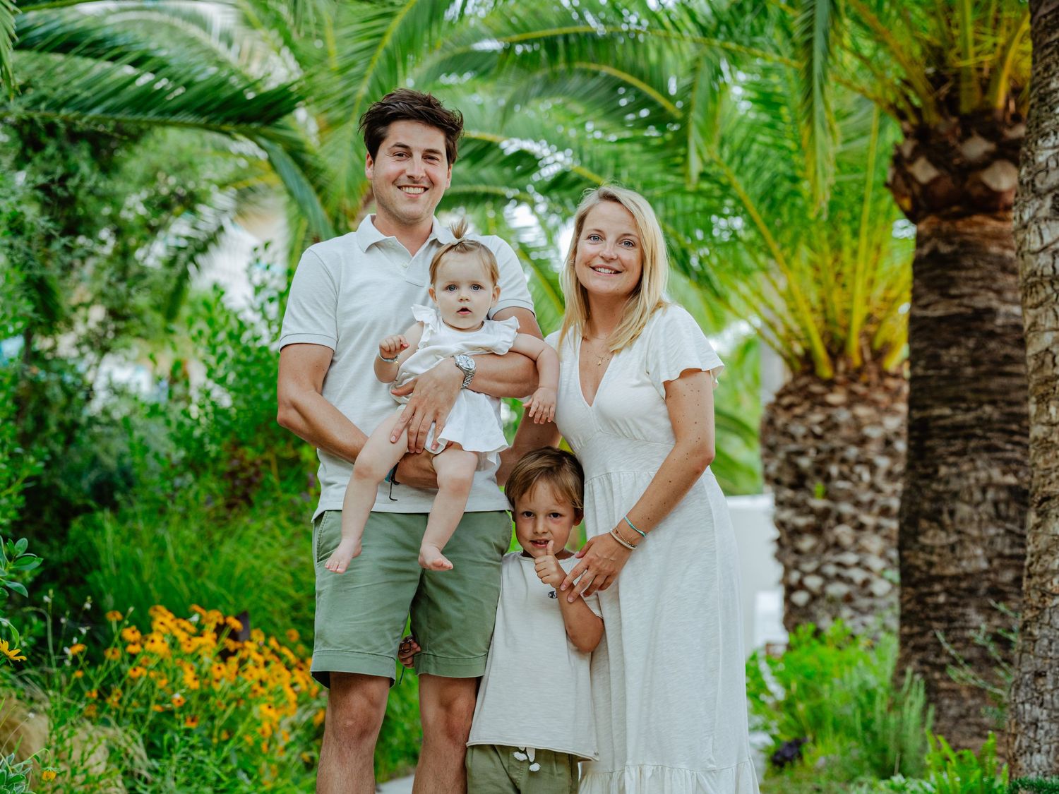 Happy family of four posing under palm trees outdoors.