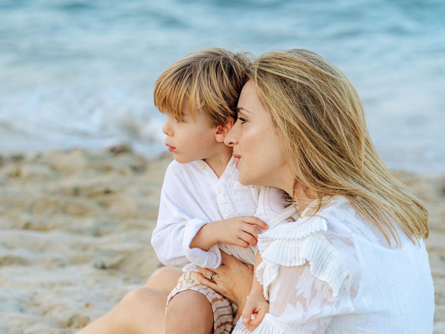 Mother and young child sharing a tender moment together on a sandy beach by the ocean.