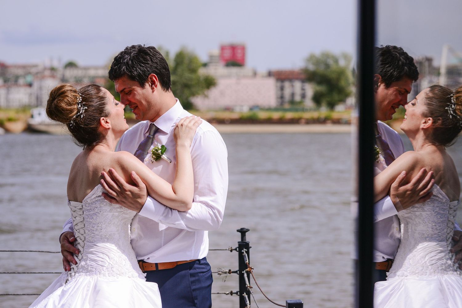 Wedding couple embracing near waterfront with mirror reflection doubling the romantic moment.