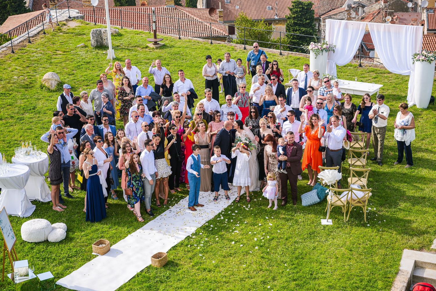Aerial view of wedding guests gathered on a green lawn at an elegant outdoor wedding reception.